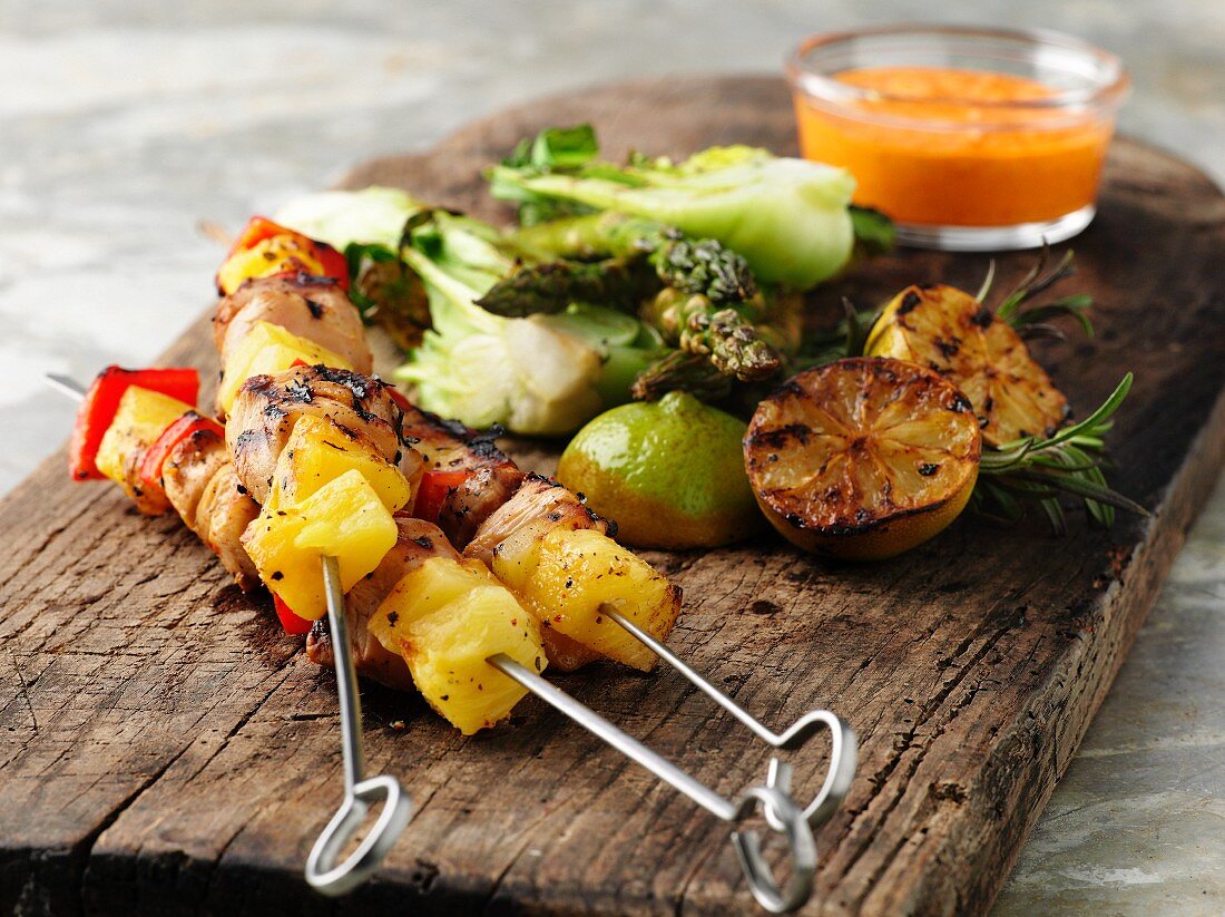 Grilled chicken skewers with lemons and vegetables on a wooden board