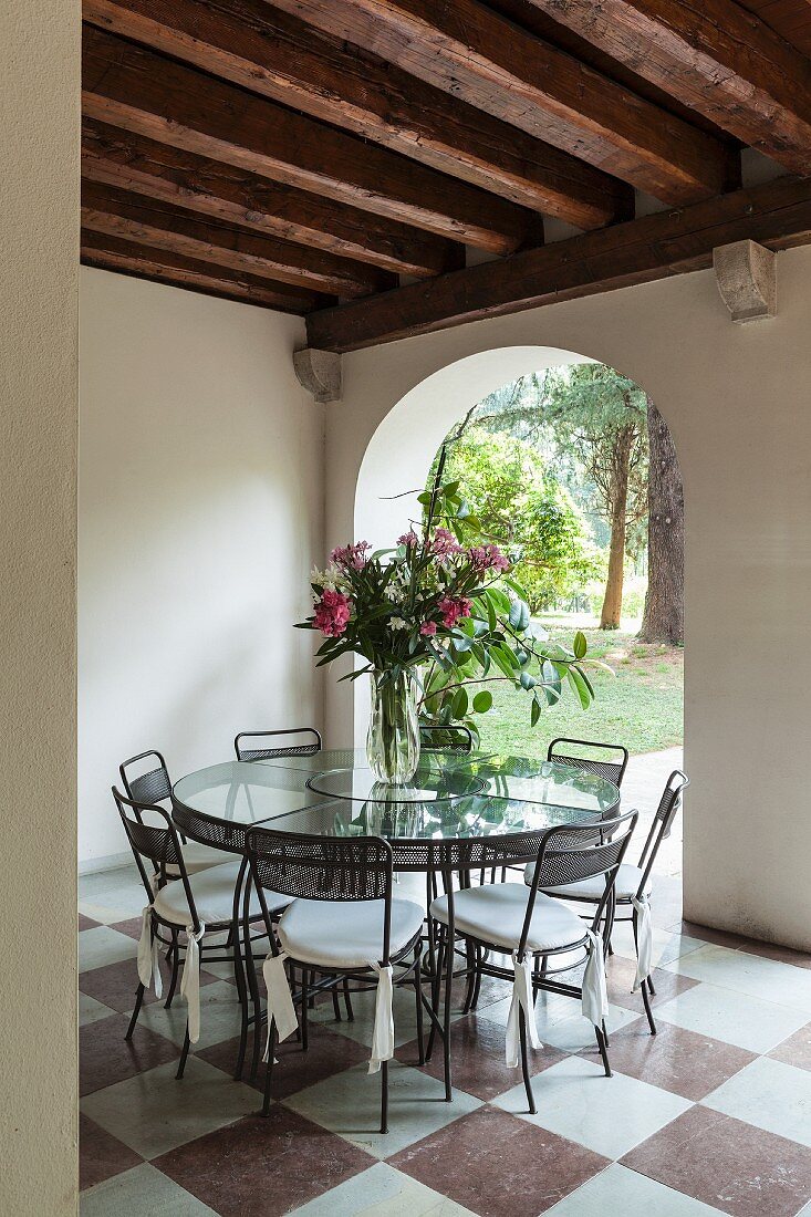 Chairs around glass table on marble floor in front of archway with view of garden