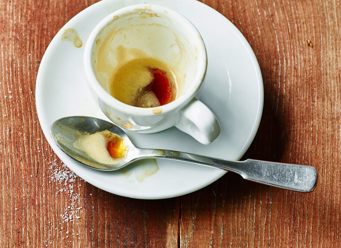 The remains of espresso and an espresso cup and on a spoon on a saucer