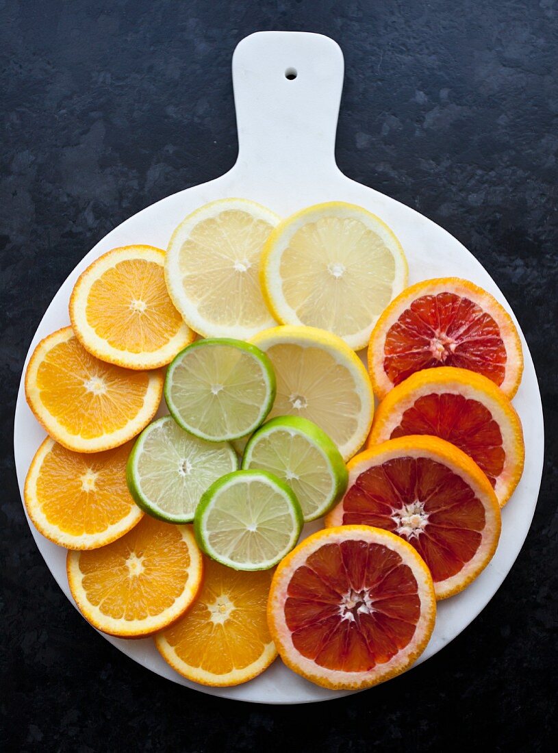 Zitronen-, Limetten-, Orangen- und Blutorangenscheiben auf weißem Tablett (Draufsicht)