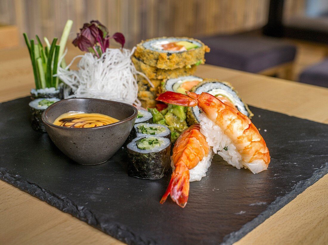 Various types of sushi on a slate platter in a restaurant