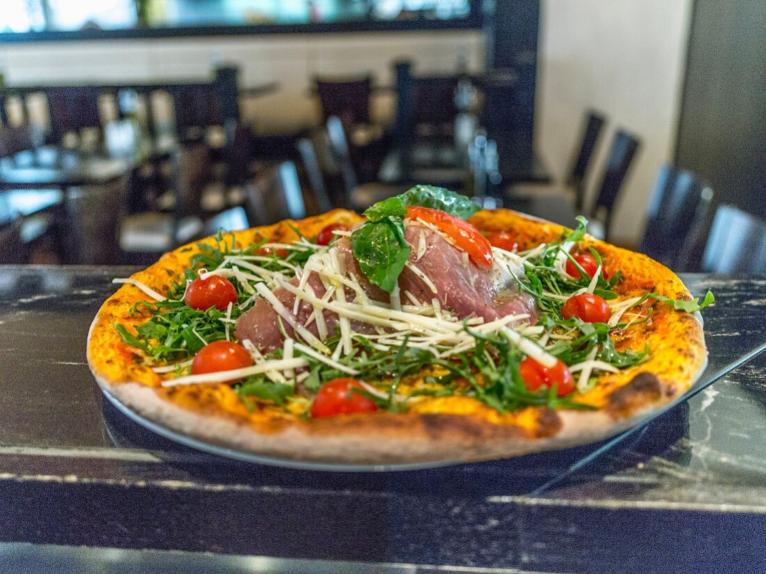 A pizza with Parma ham, rocket and cherry tomatoes on a restaurant bar