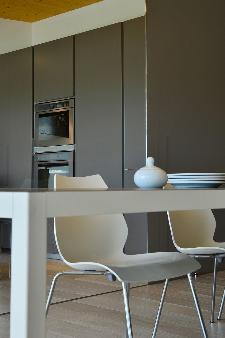 View across edge of table to white shell chairs and fitted kitchens