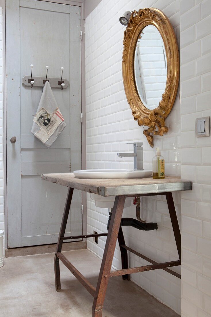 Rustic washstand below gilt-framed mirror on white-tiled wall
