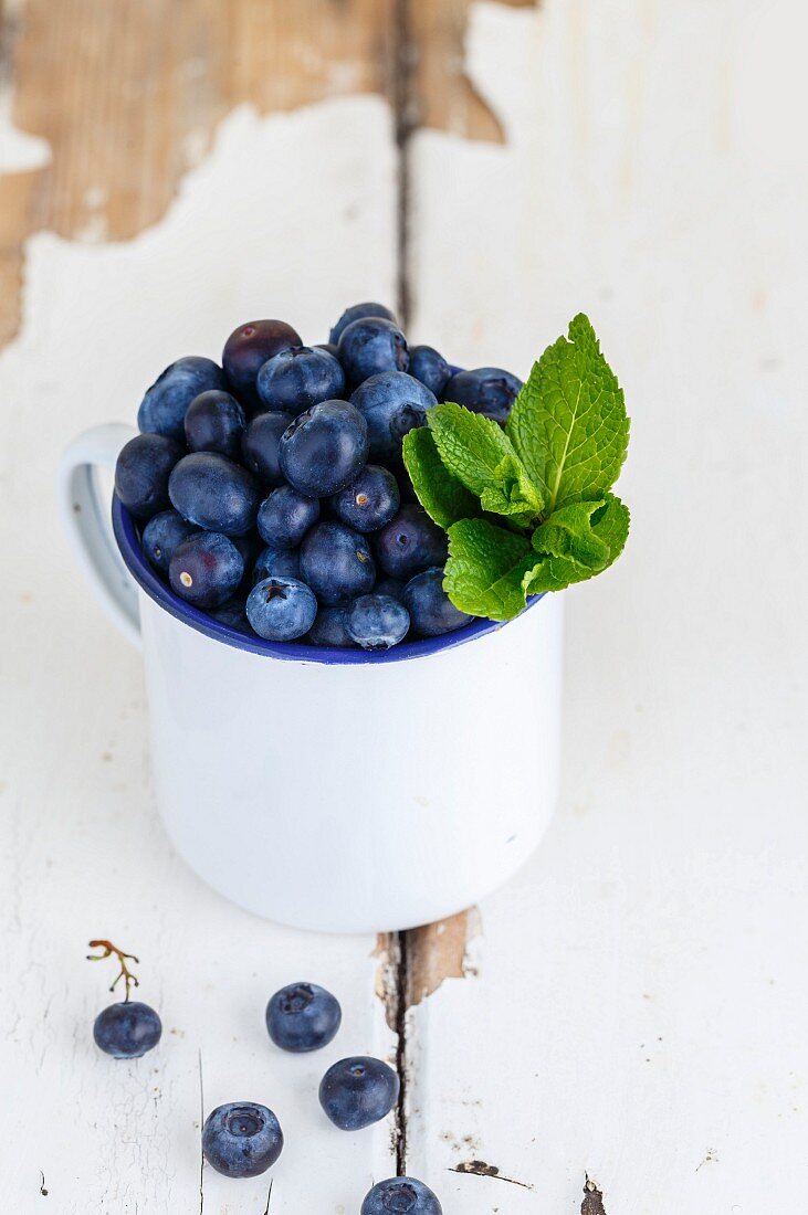 Blueberries and peppermint leaves in a white enamel cup