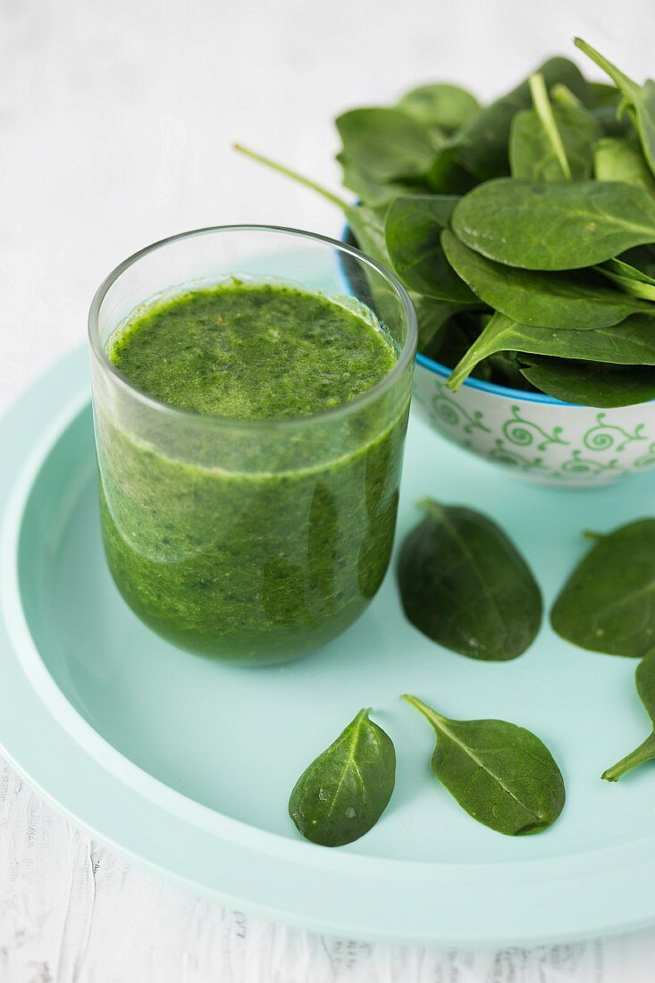 A spinach smoothie in a glass with fresh spinach