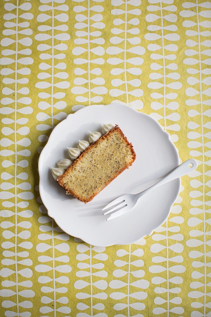 Ein Stück Zitronen-Mohn-Kuchen mit Frischkäseglasur auf weißem Teller mit Gabel