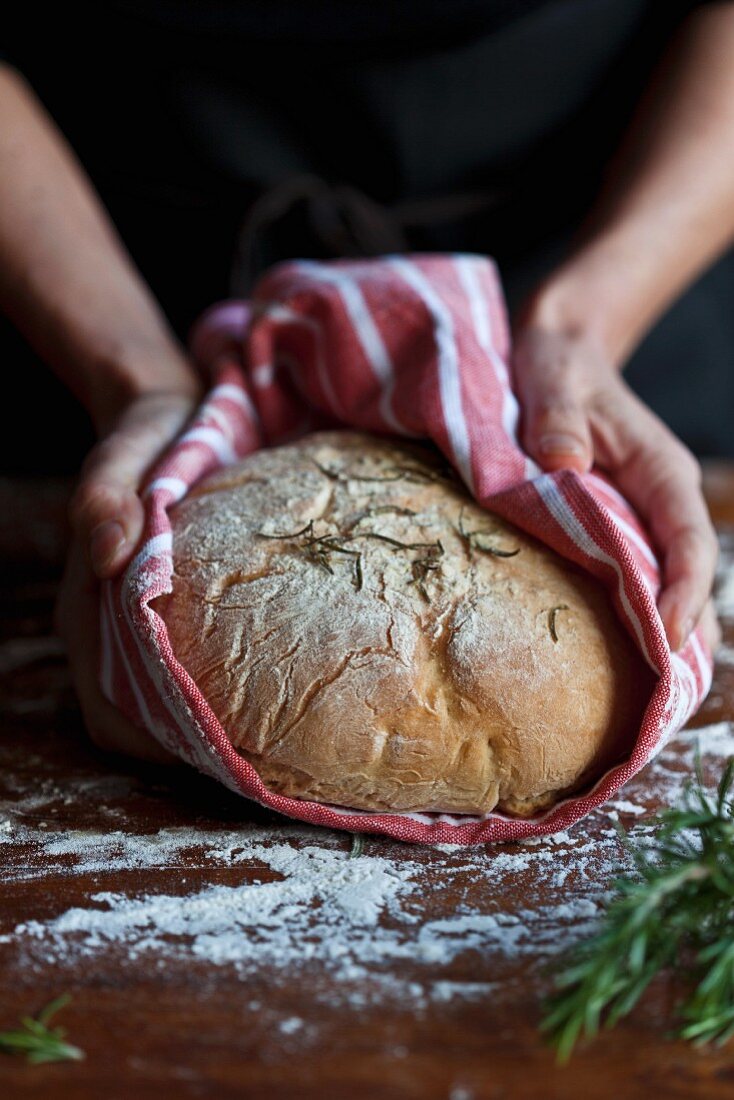 Hände halten frisch gebackenes Brot im Geschirrtuch