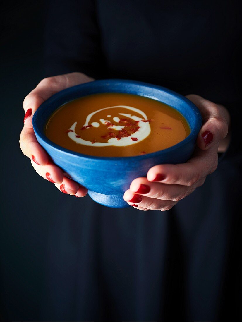 A woman holding a bowl of cream of pumpkin soup