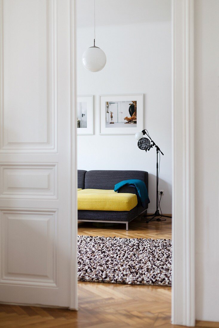 Offene weiße Flügeltür in Altbauwohnung mit durchgehendem Fischgrätparkett, Blick ins Wohnzimmer mit Stehleuchte neben modernem Sofa