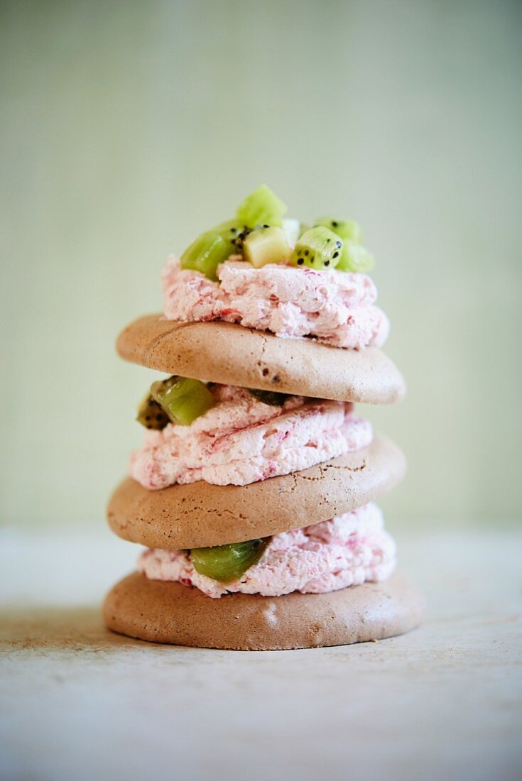 A stack of meringue biscuits with strawberry cream and kiwis