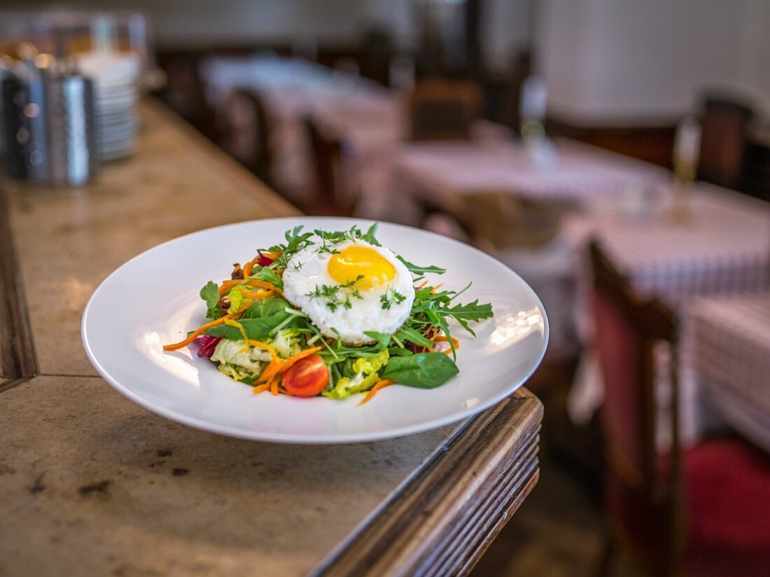 A mixed salad with a fried egg on a restaurant counter