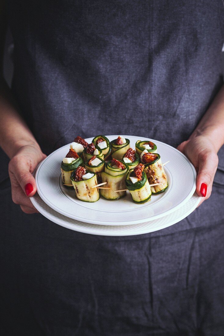 Frau hält gegrillte Zucchiniröllchen mit Mozzarella und getrockneten Tomaten