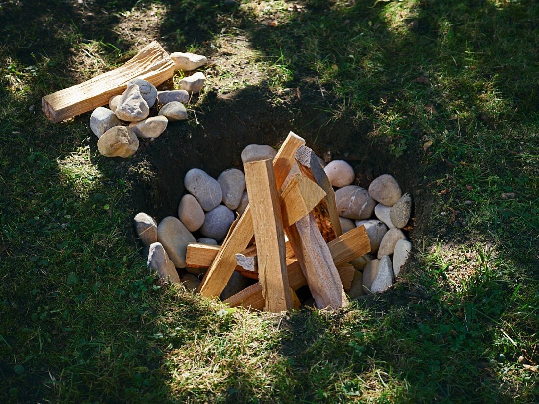 Für Luau-Grillfest - Grube mit Steinen und Brennholz ausgelegt
