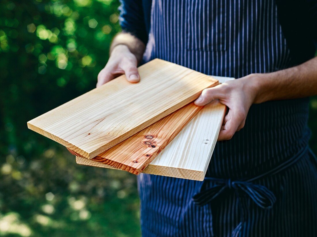 Mann präsentiert verschiedene Holzbretter zum Grillen