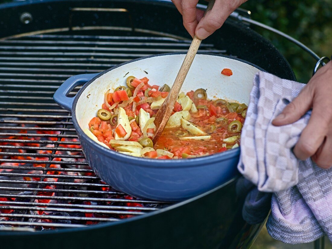 Tomato and artichoke sauce being heated on a glowing coals