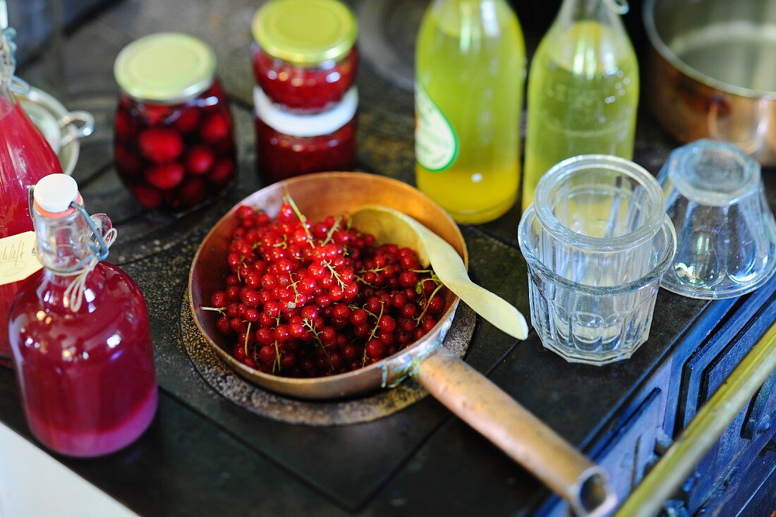 Verschiedene selbstgemachte Obstsäfte, eingelegte Früchte und frische Johannisbeeren auf altem Küchenherd