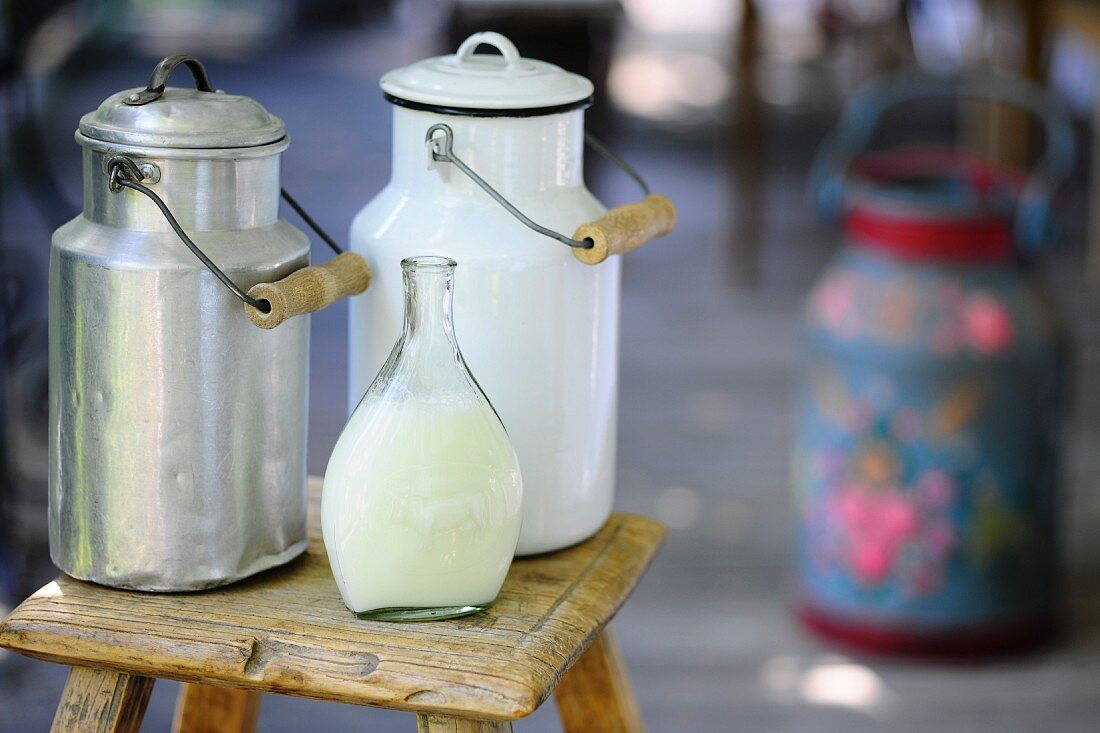 Milk churns and a bottle of milk on a wooden stool