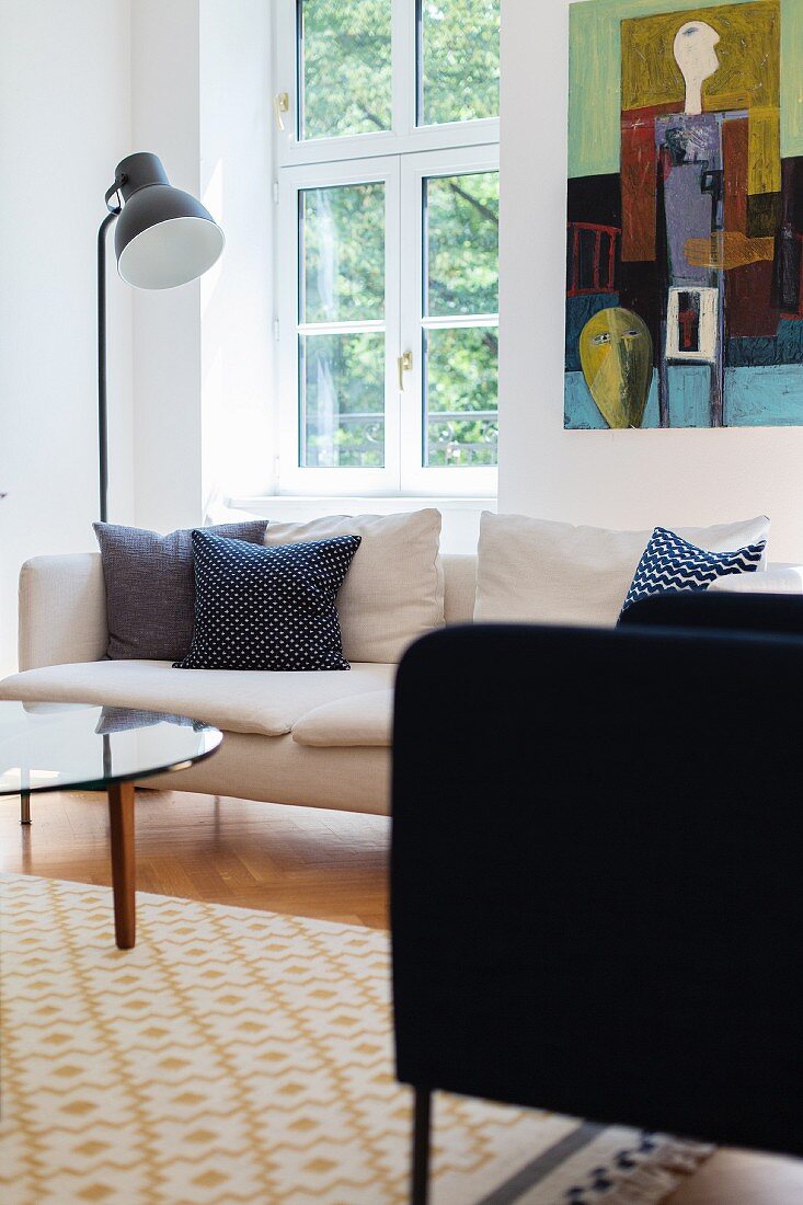 Armchair and standard lamp next to white sofa below lattice window and modern artwork