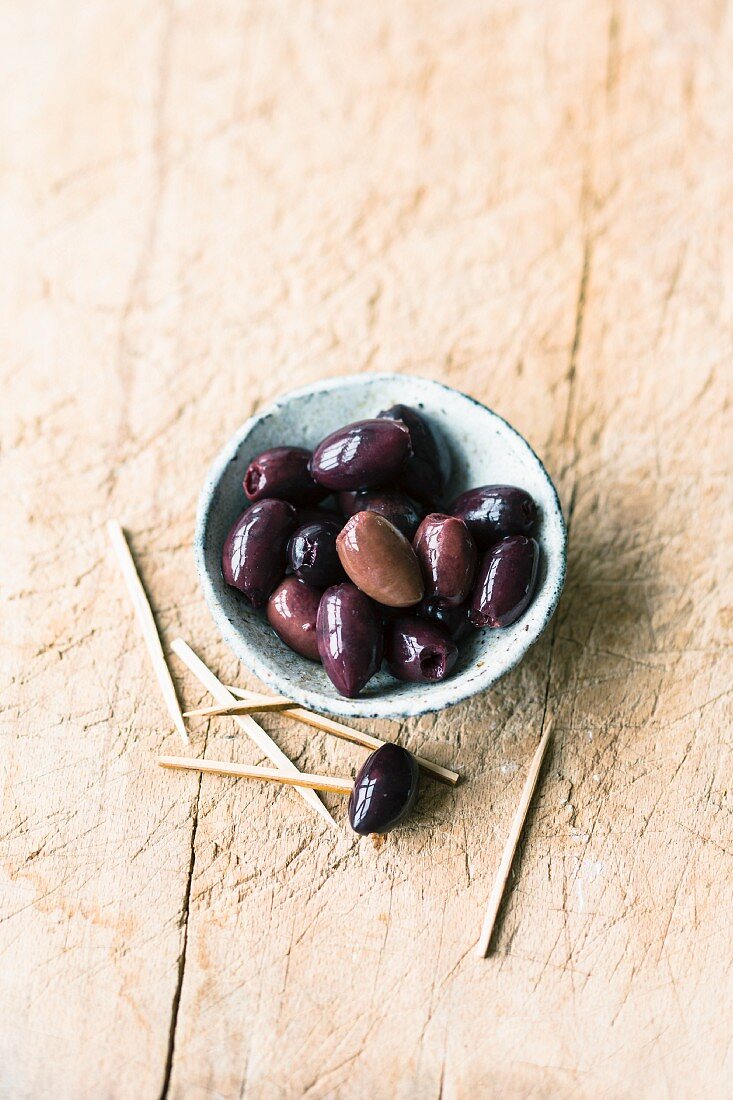 A bowl of black olives with toothpicks next to it