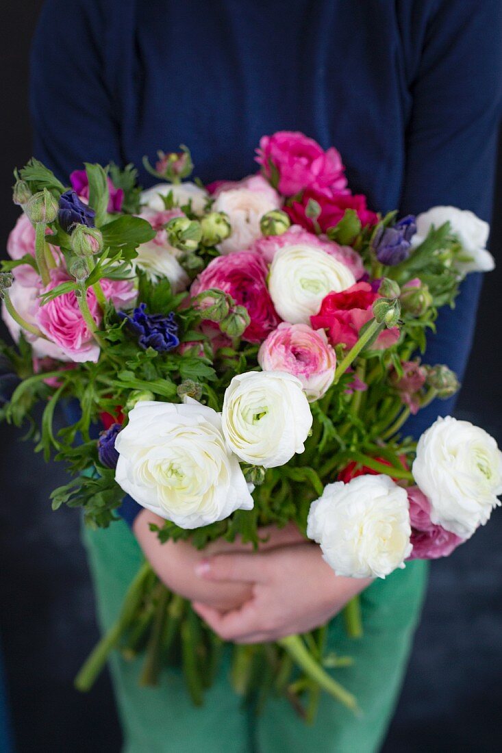 Hände halten Blumenstrauss mit Ranunkeln und Anemonen