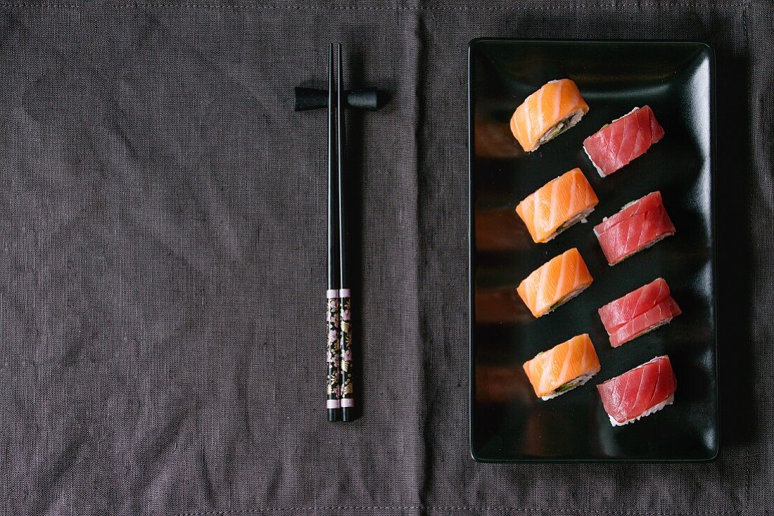 Sushi mit Lachs und Thunfisch auf schwarzem Teller, daneben Essstäbchen (Japan)