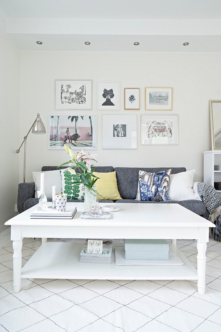 White rustic coffee table in front of grey sofa with scatter cushions below gallery of pictures