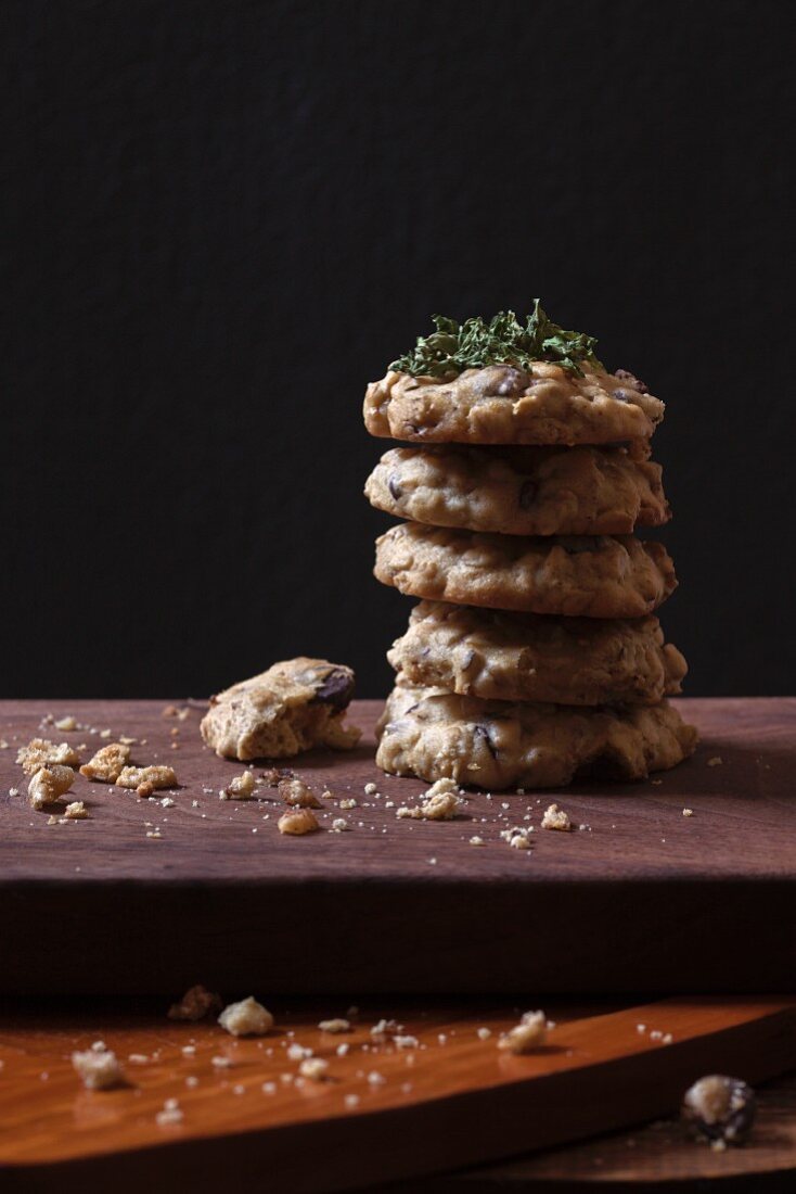 A stack of homemade chocolate chip oat biscuits on a wooden board