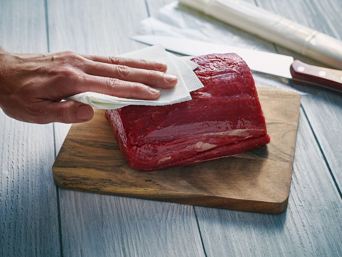 A piece of beef being patted with kitchen paper
