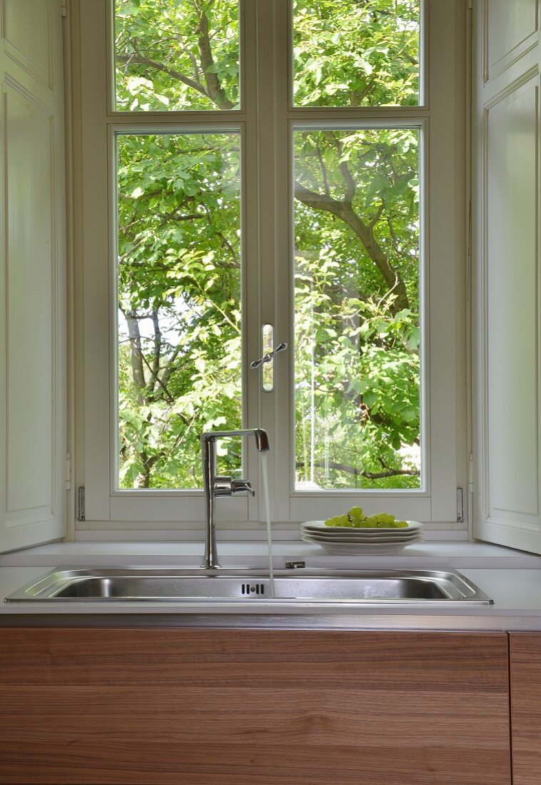 Water running from tap into sink below lattice window with view into garden