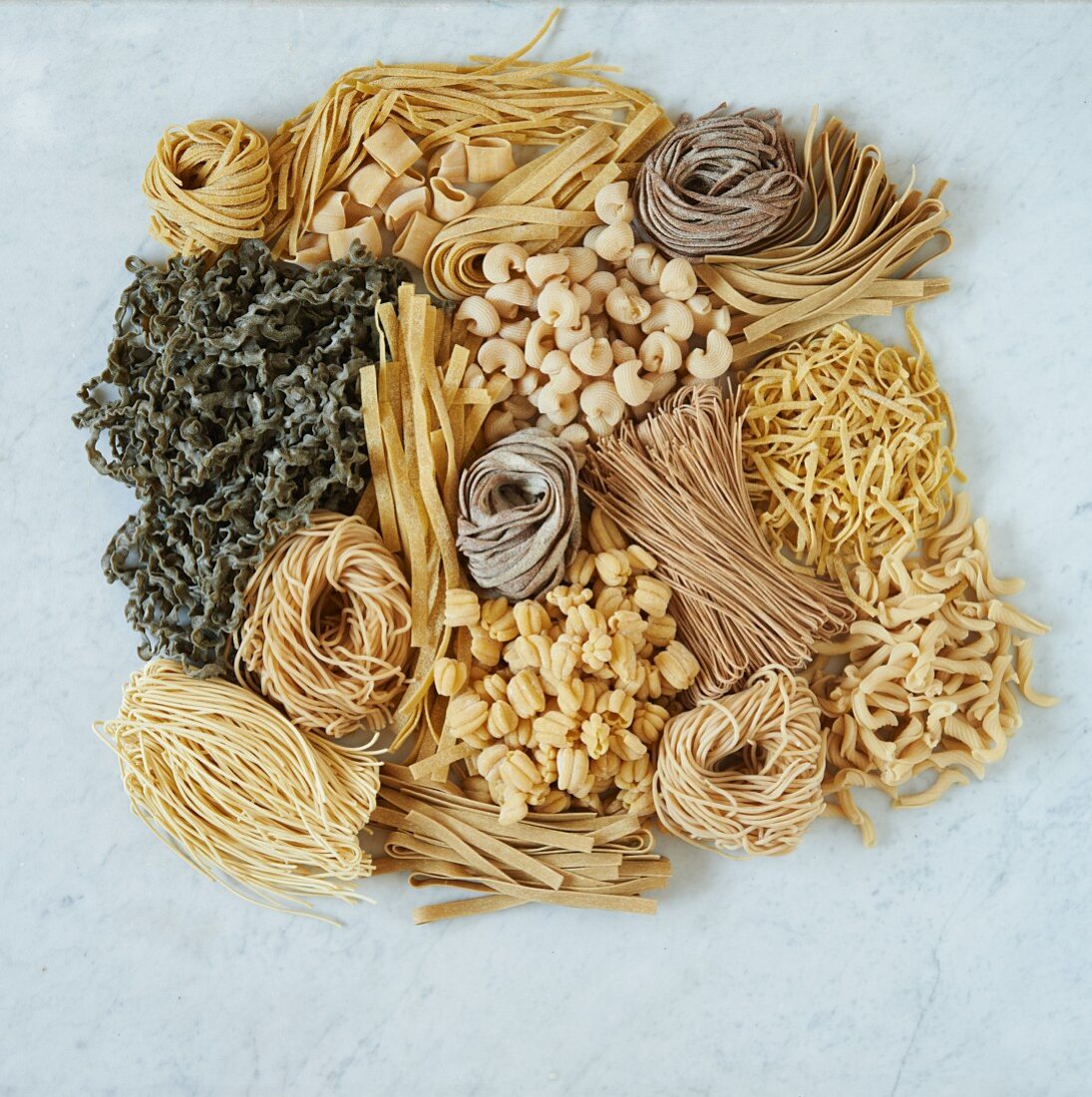 Various types of pasta on a white surface (seen from above)
