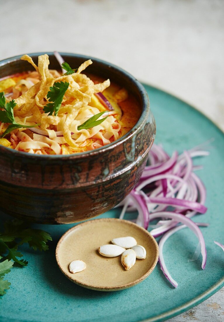Khao Soi soup garnished with red onions, limes, pumpkin seeds and coriander