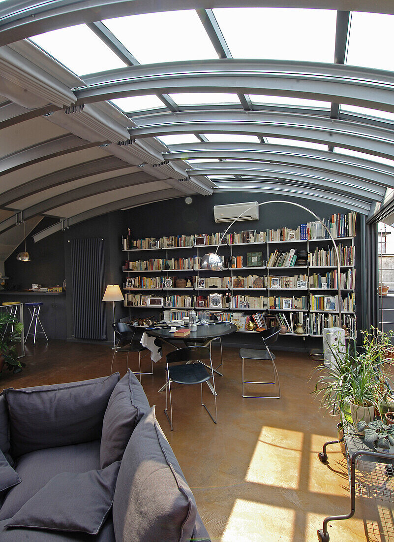 Bookcase, dining area and lounge in open-plan interior with metal and glass elements