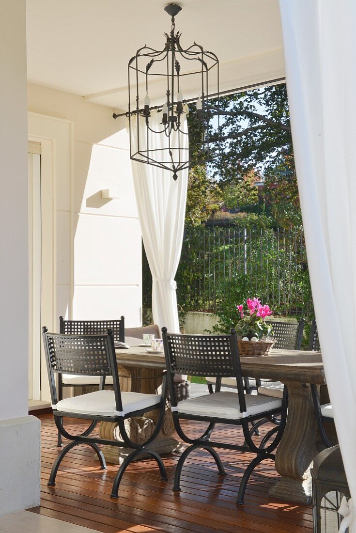 Stone table and wrought iron chandelier in elegant loggia seating area with garden view