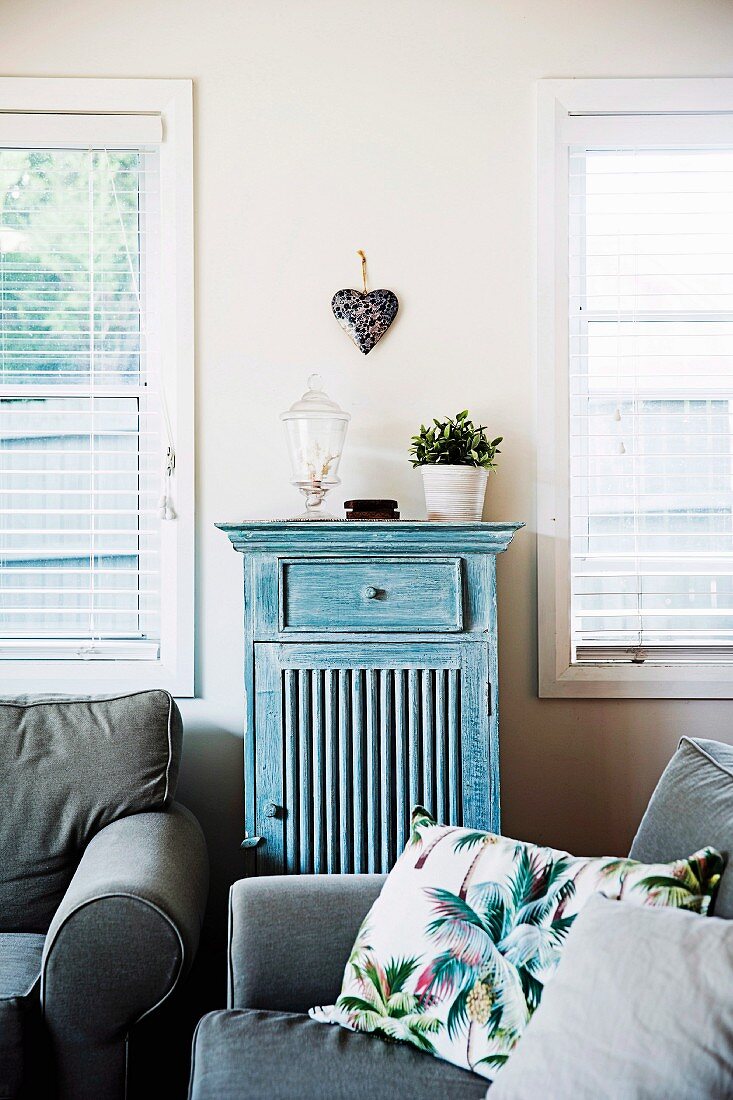 Gray upholstered furniture in front of windows with a half-height vintage cupboard and decorative heart