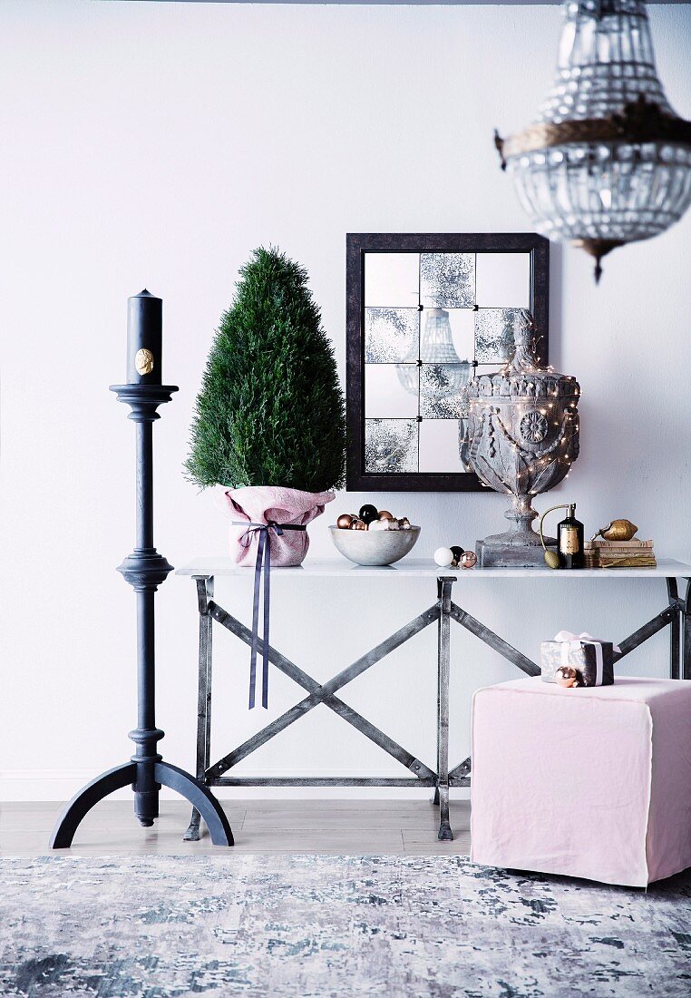 Christmas arrangement with ornamental trees, Christmas balls and fairy lights on a console table next to a turned candlestick