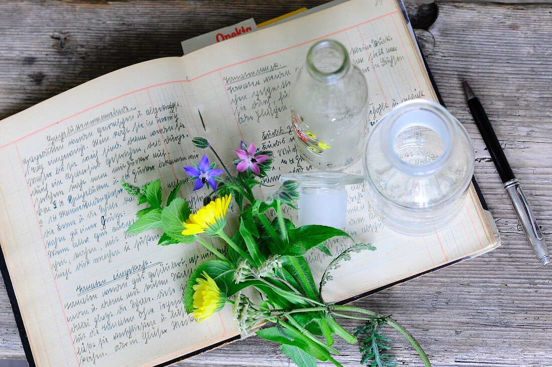Wiesenblumen und Apothekerflasche auf aufgeschlagenem Rezeptbuch