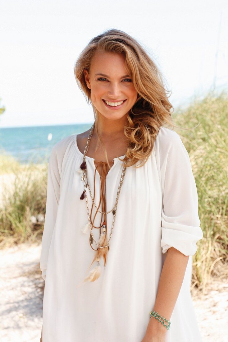 A young blonde woman on a beach wearing a white tunic