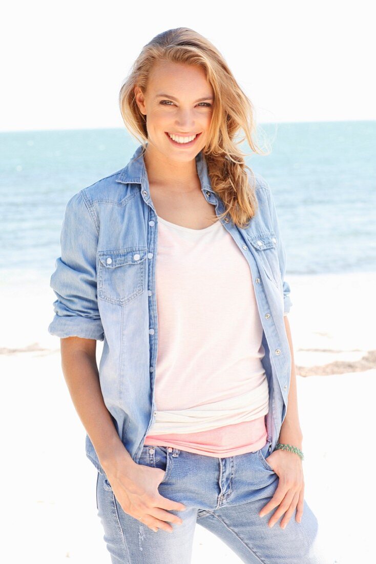 A young woman wearing tops, a denim shirt and jeans on a beach