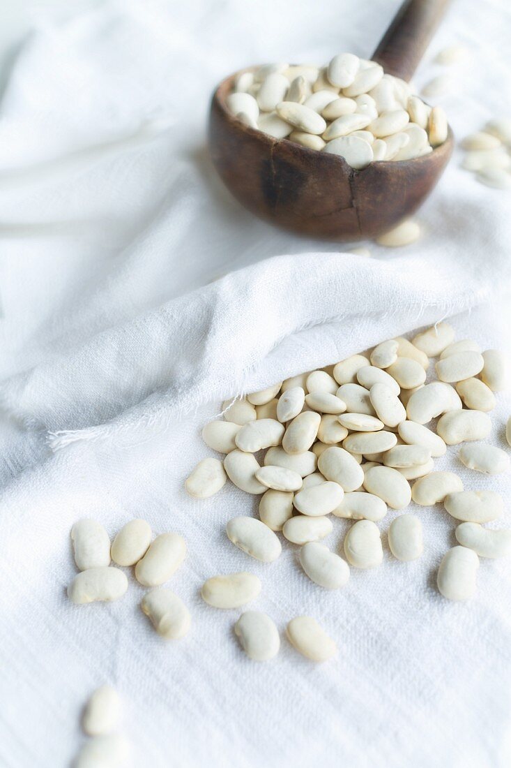 Dried white giant beans (organic) on an old wooden ladle and on a piece of linen