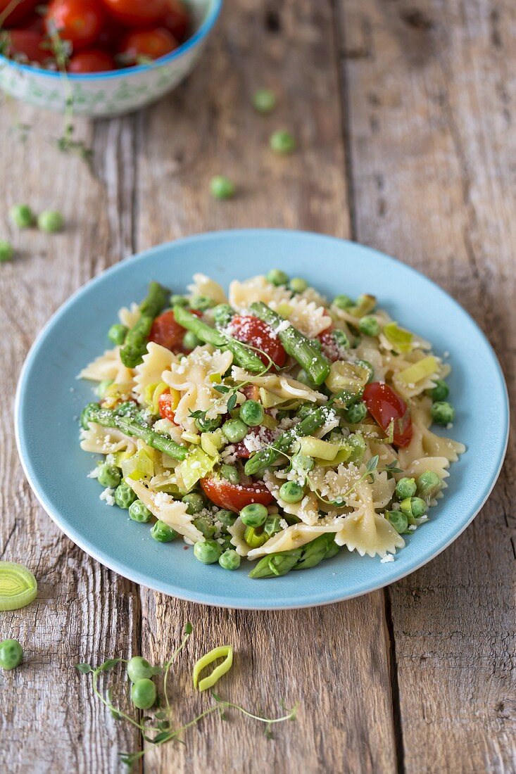 Pasta Primavera with asparagus, peas, leek and tomatoes on wooden surface