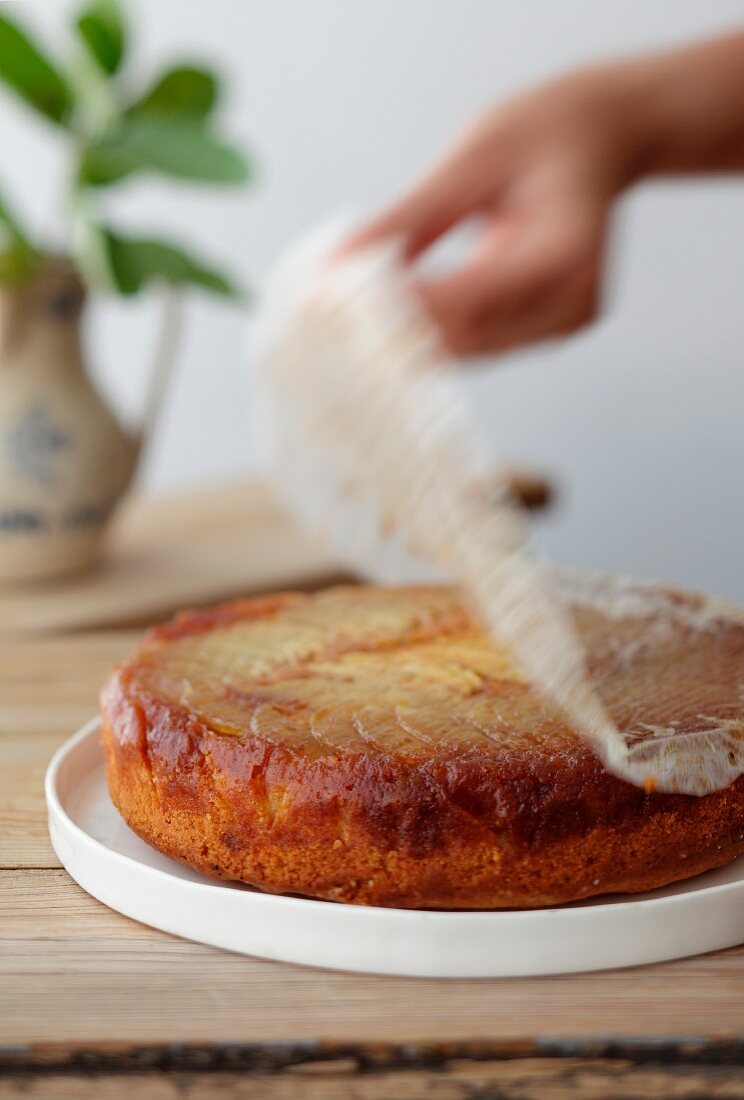 A hand removing parchment paper from an apple cake