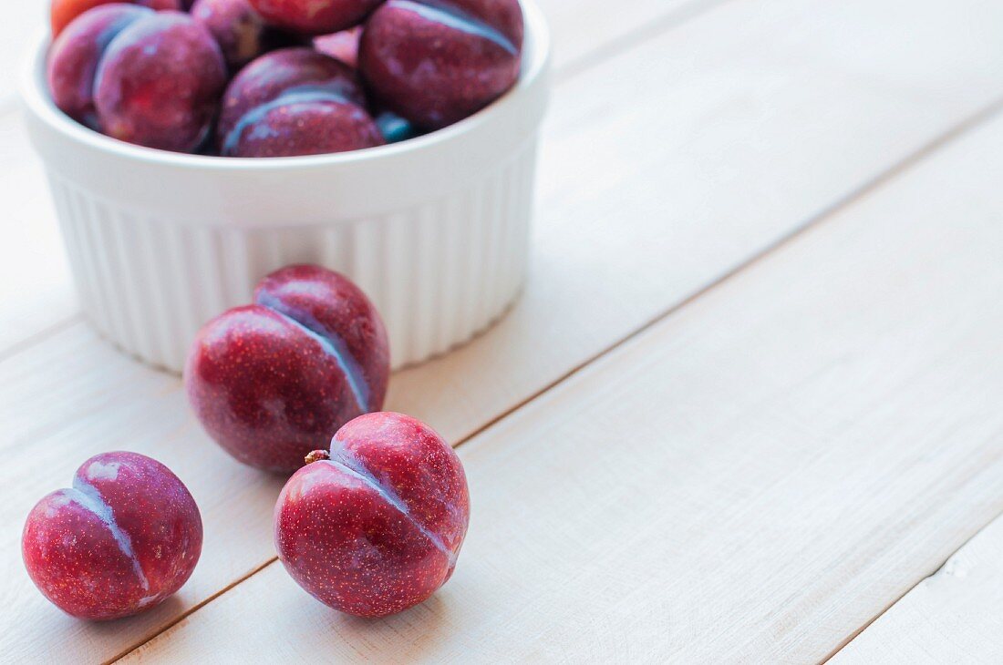 Plums in a bowl and on a wooden surface