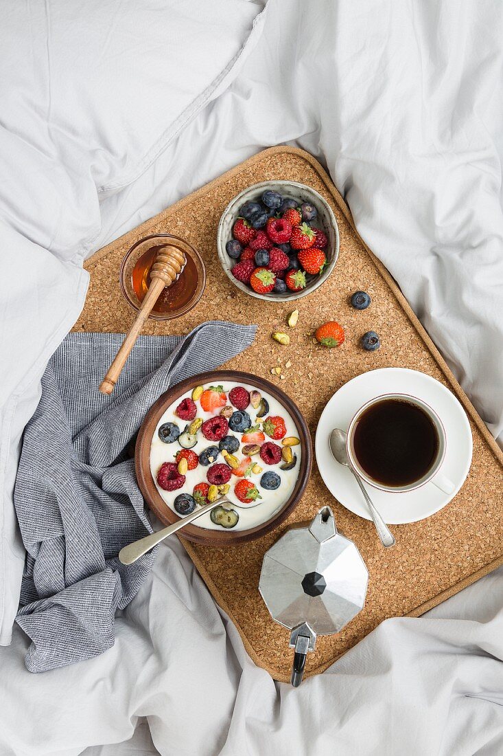 Frühstückstablett mit Kaffee, Beerenjoghurt, Honig und frischen Beeren