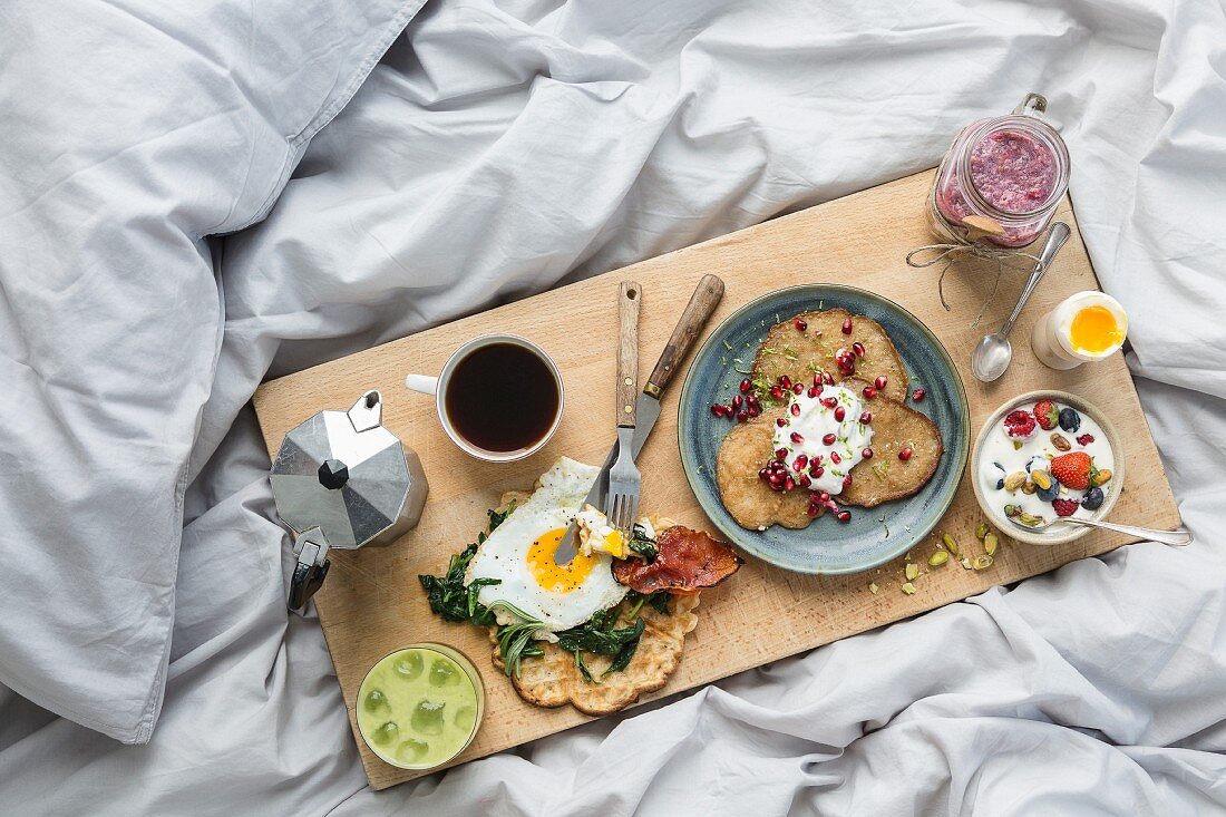 Coffee and various dishes on a wooden board on a white duvet