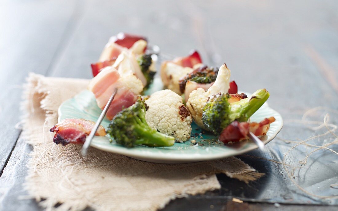 Gegrillte Blumenkohl-Brokkoli-Spiesse mit Speck auf Teller