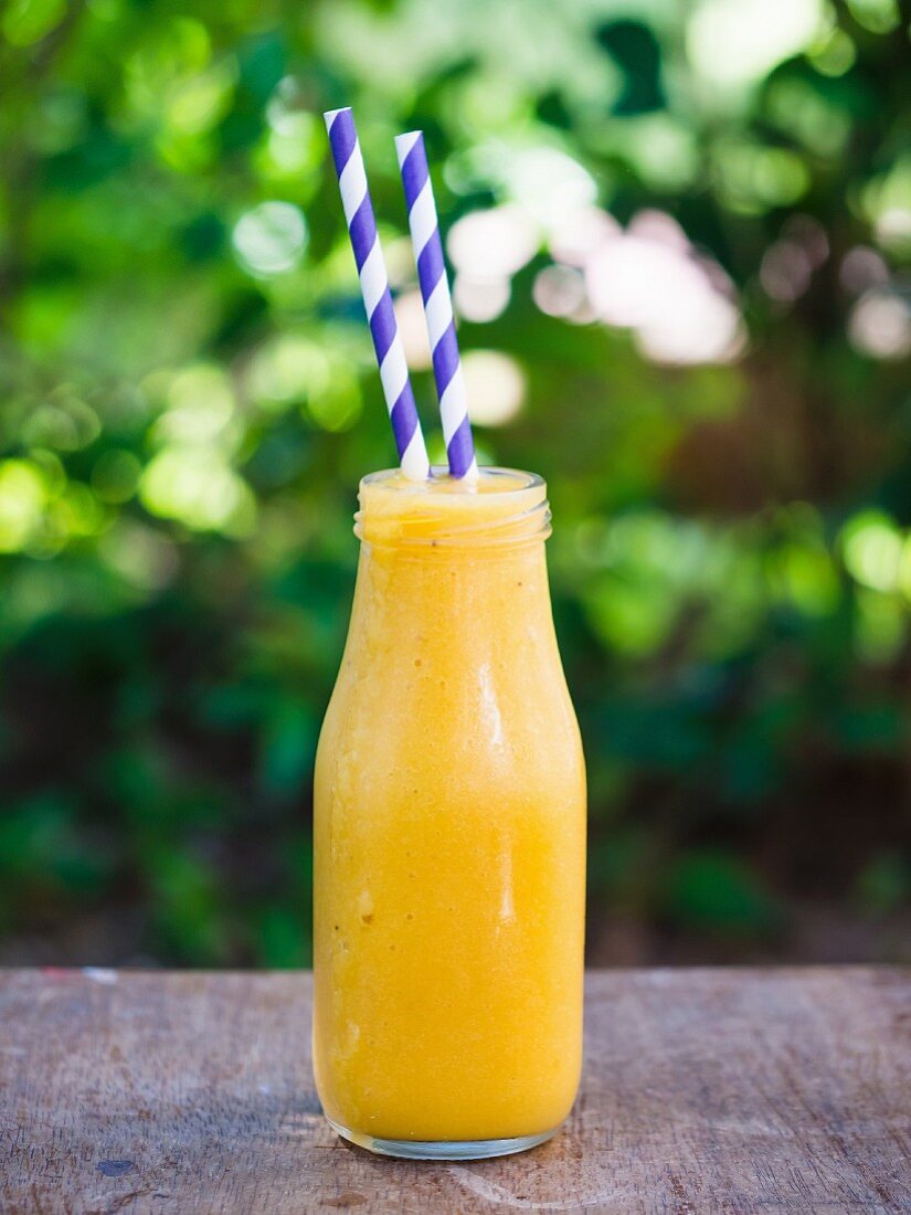 Gelber Mango-Ananas-Smoothie in Flasche auf Gartentisch