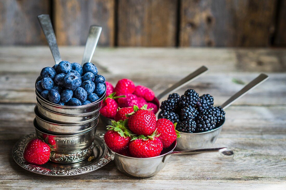 Frische Beeren in Silbergeschirr auf rustikalem Hintergrund