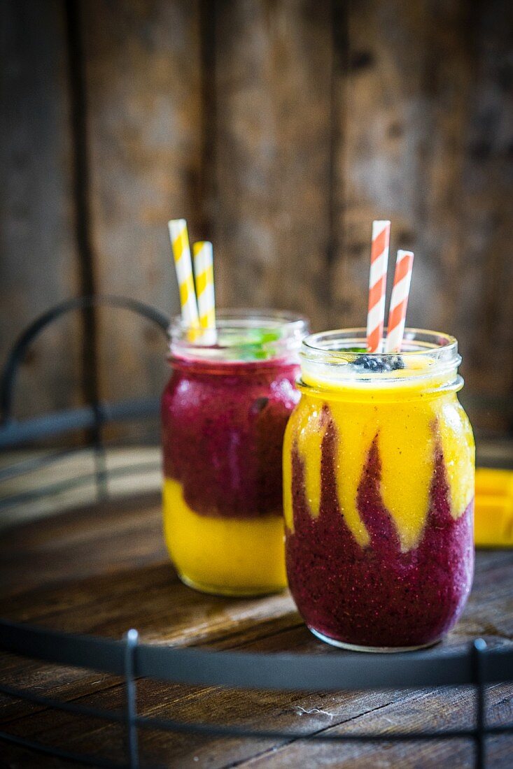 Colourful two layer mango and berry smoothies garnished with blackberries