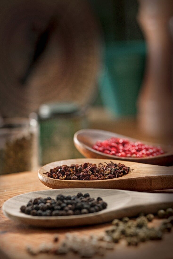 Various types of peppercorns on wooden spoons
